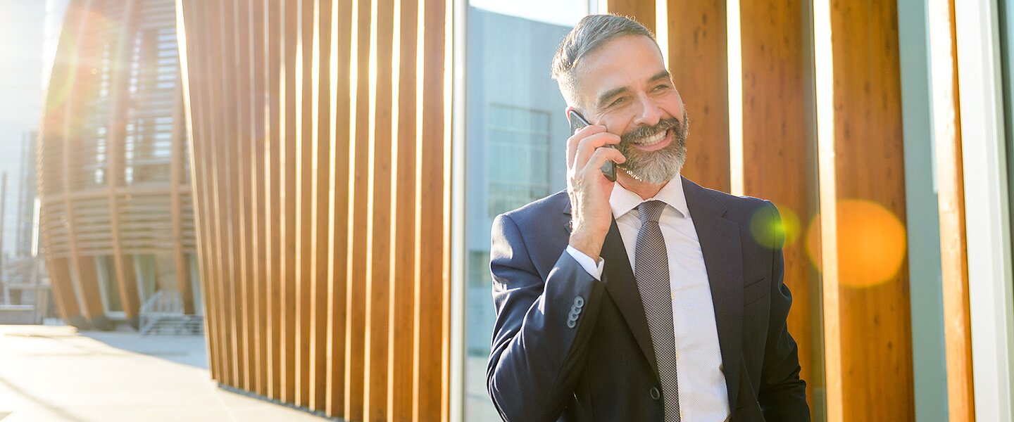 Ein Immobilienmakler, der vor einem Haus steht und einem potenziellen Kunden am Telefon die Vorzüge der Produkte NettoImmo und SystemImmo erläutert