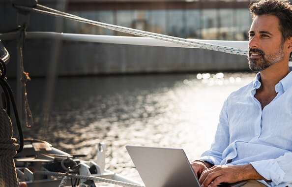 Ein freier, unabhängiger Versicherungsmakler, der mit Laptop am Wasser sitzt