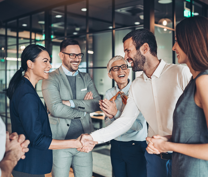 Gut gelaunte Mitarbeiterinnen und Mitarbeiter im Büro, die sich die Hand reichen