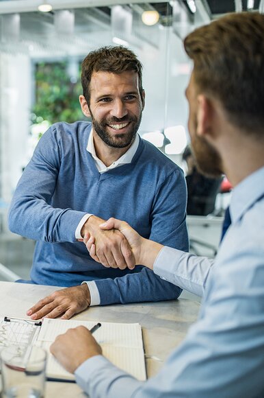 Ein Fonds Finanz Mitarbeiter gratuliert einem Vermittler zum Unterzeichnen der verschiedenen Bestandteile des Vertragspakets