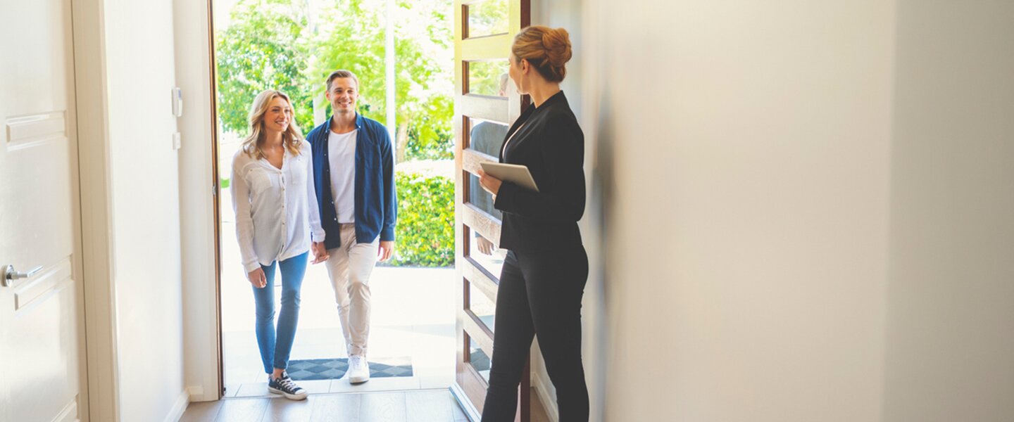 Eine Immobilienmaklerin empfängt Kunden an der Haustür einer Immobilie