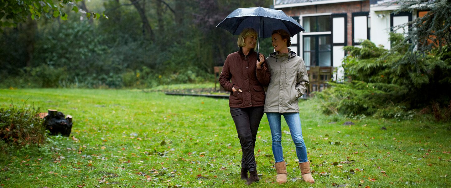 Eine Mutter und ihre Tochter mit Regenschirm im Garten hinter ihrem Haus